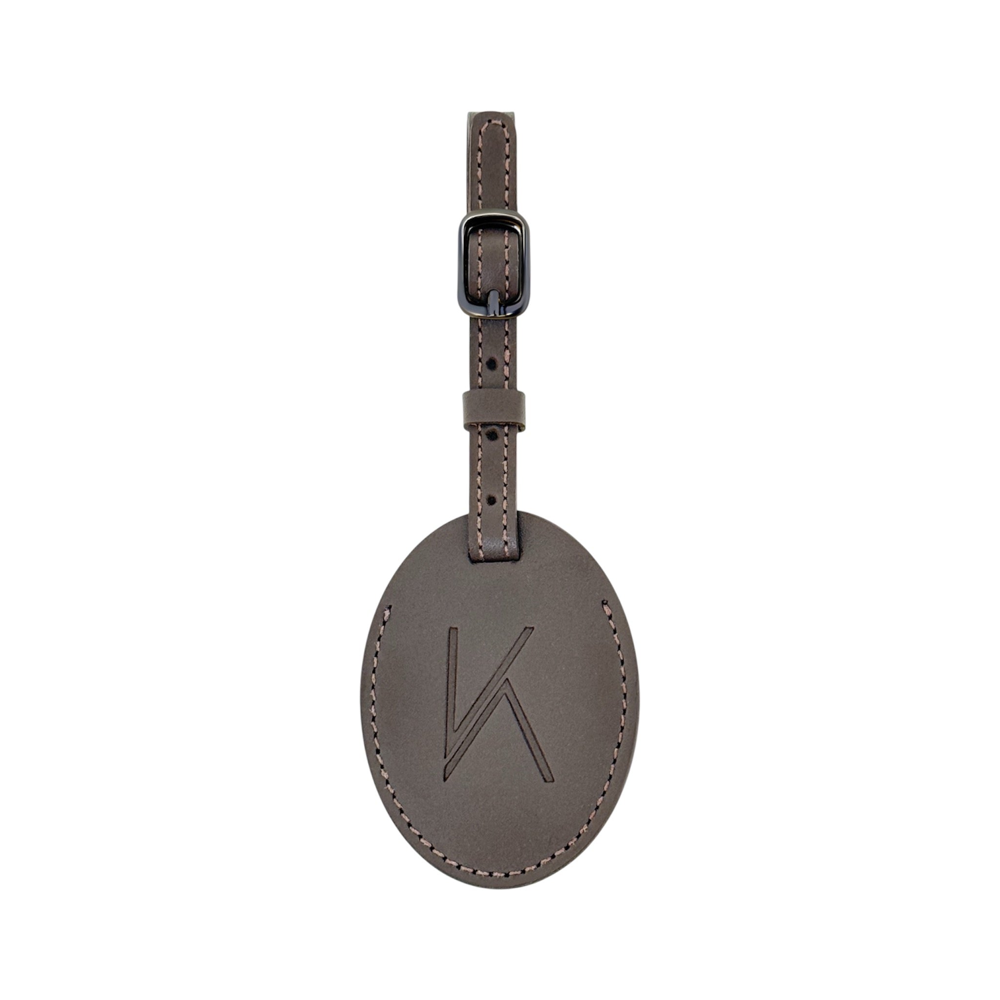 A brown oval leather luggage tag with a matching strap and buckle, featuring an embossed stylized 'K' logo on the front, shown against a plain white background.