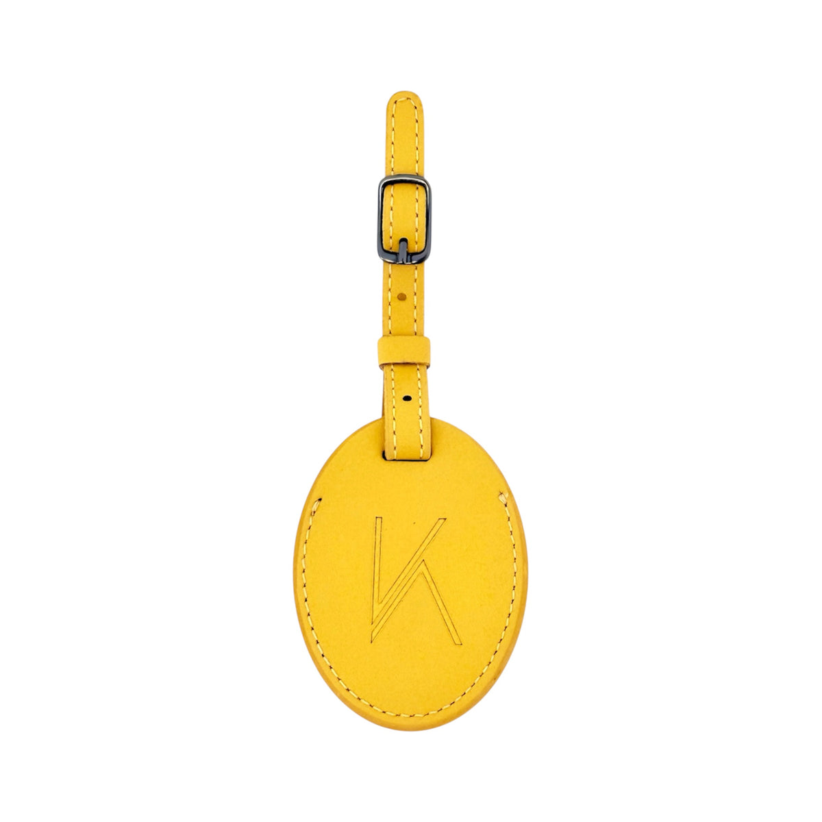 A mustard oval leather luggage tag with a matching strap and buckle, featuring an embossed stylized 'K' logo on the front, shown against a plain white background.